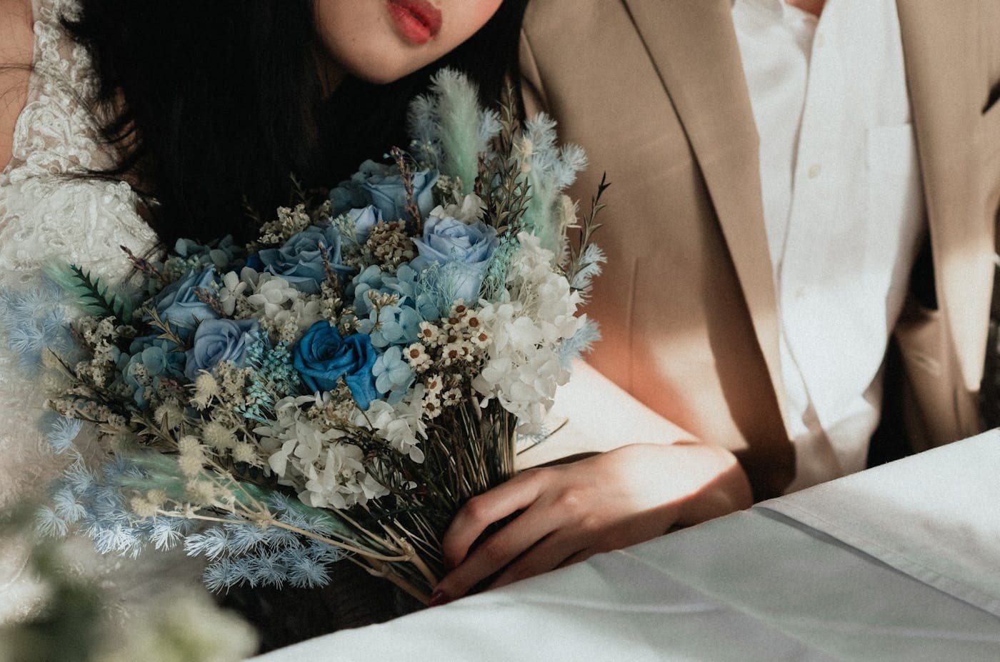 A bride in a pale suit holding a dried bouquet of blue and white flowers