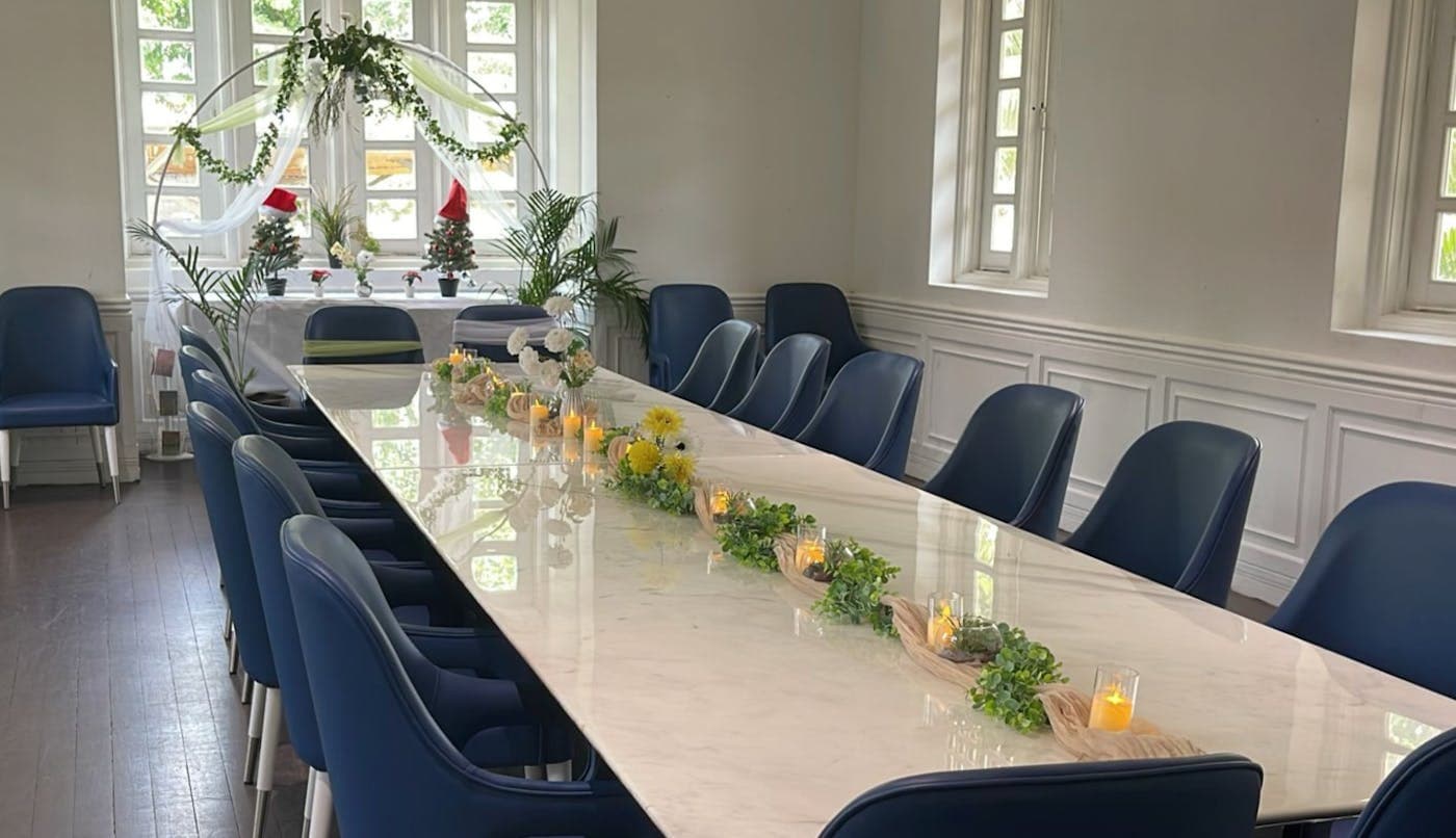 A long white table laid for a private event, navy chairs and a runner of greenery and candles