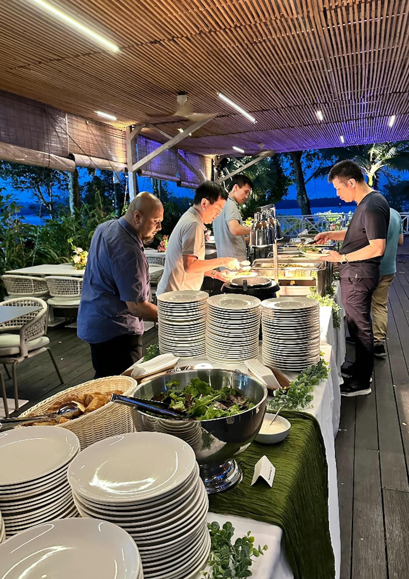 Guests serving themselves along a buffet line at dusk, stacked plates in the foreground