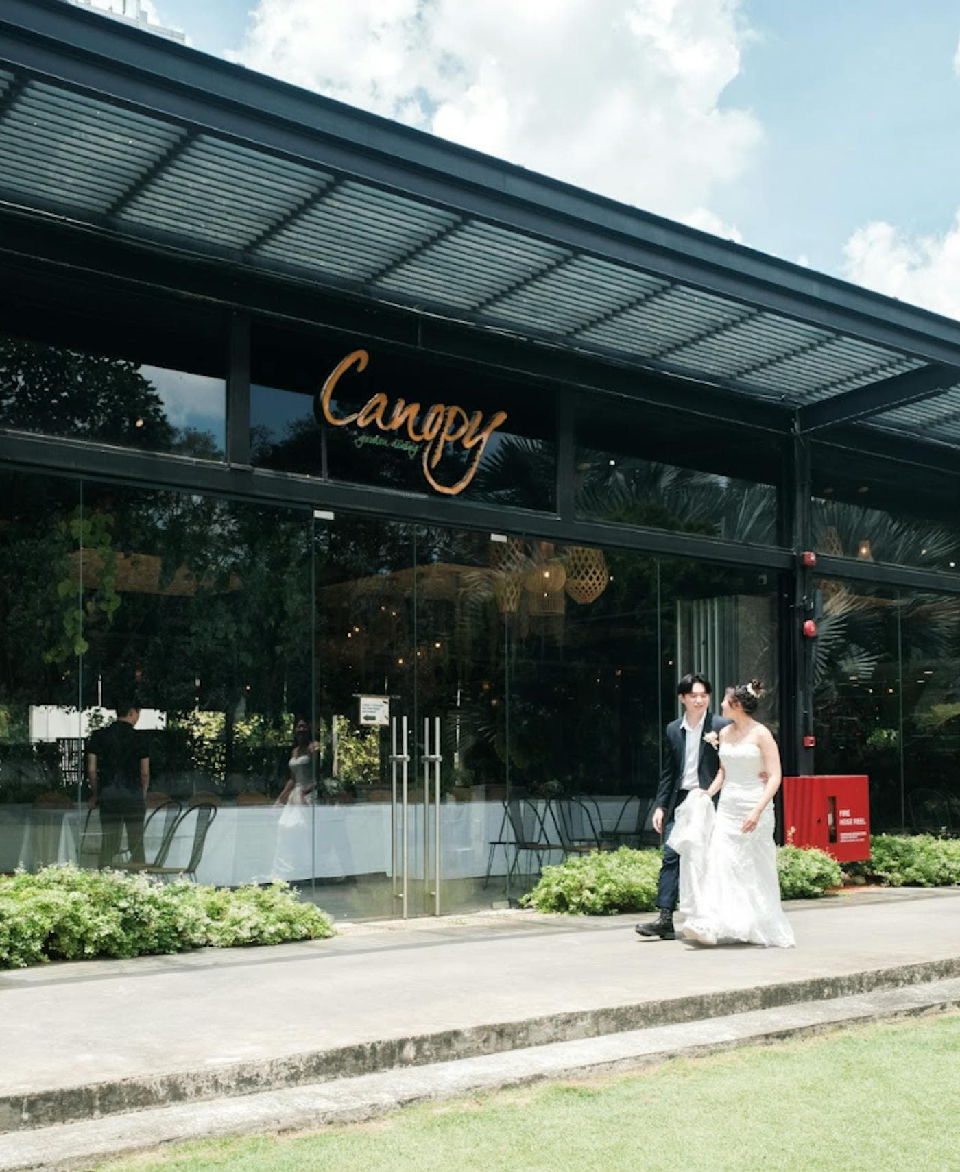 A bride and groom outside the glass frontage, beneath the Canopy sign