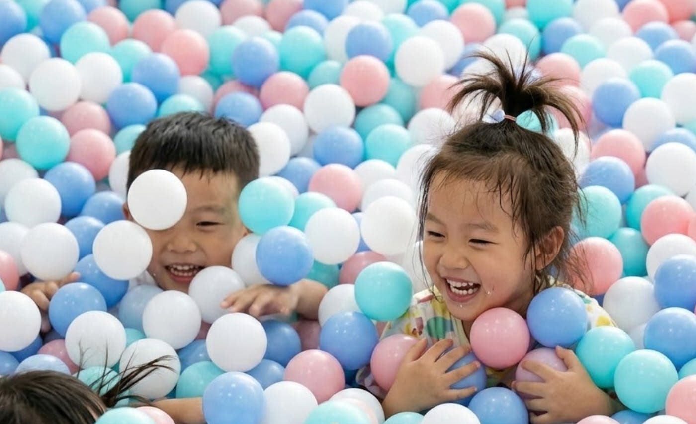 Two children laughing among the balls in a pastel ball pit