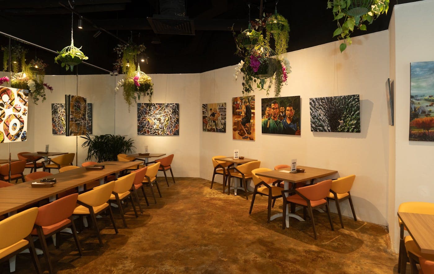 An indoor dining room with framed prints, orange chairs and plants hanging from the ceiling