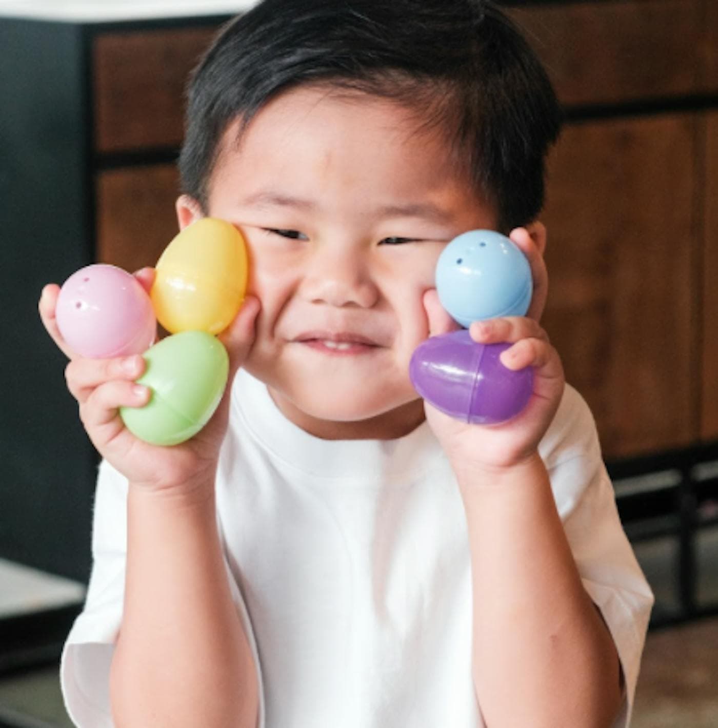 A small boy holding up four pastel plastic eggs