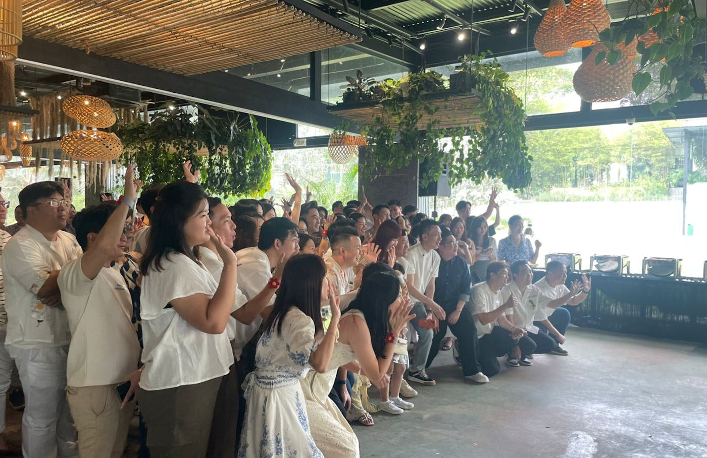 A crowd of guests dressed in white, applauding at an event under the pergola