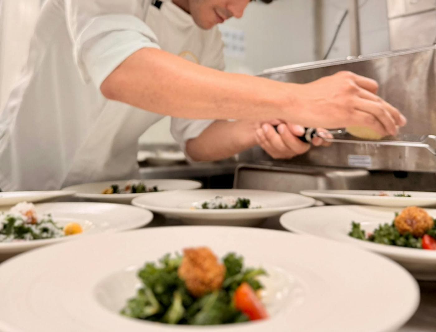 A chef plating salads into a row of white bowls