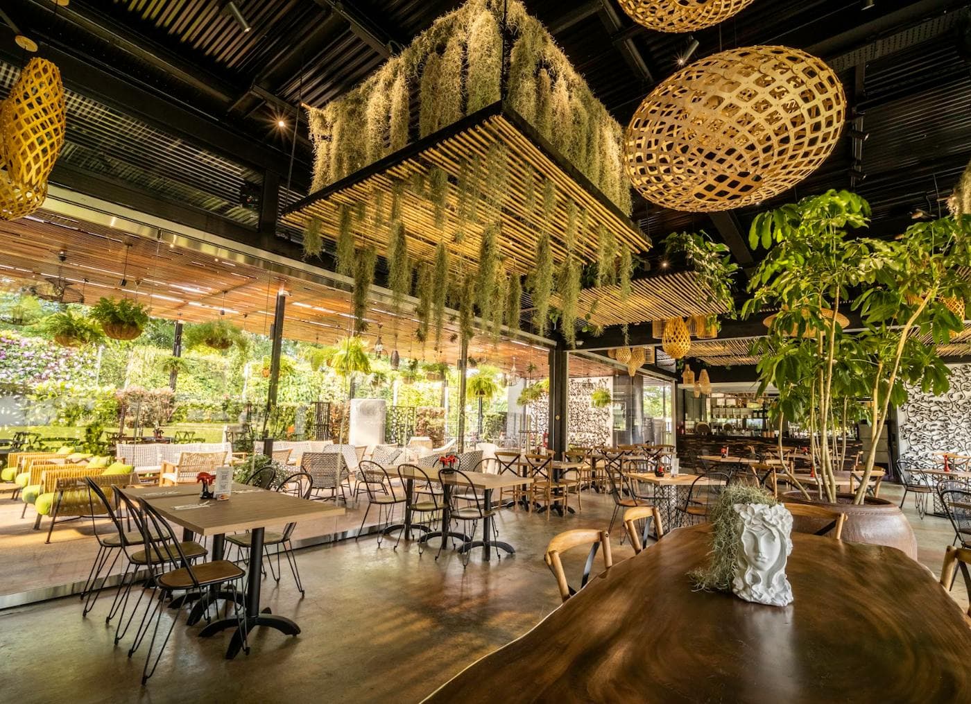 A wide dining room under woven pendant lights and hanging greenery