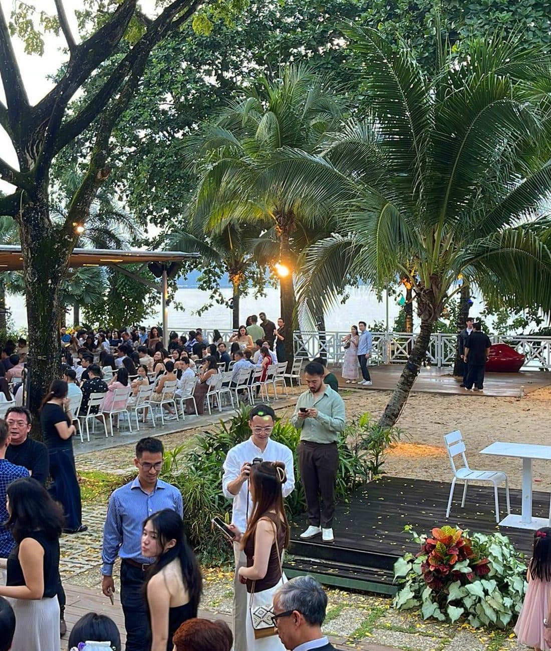 A large company gathering at Canopy Changi Village at dusk, rows of guests under the palms with the water beyond