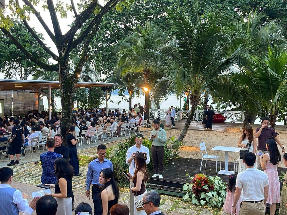 A large gathering at Canopy Changi Village at dusk, rows of chairs under the palms with the water beyond