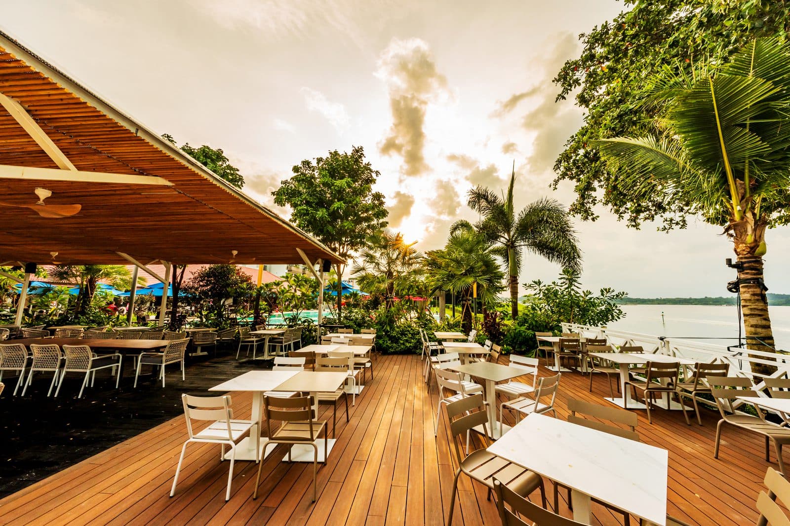 The timber deck at Canopy Changi Village at golden hour, tables set under the pavilion with the water beyond