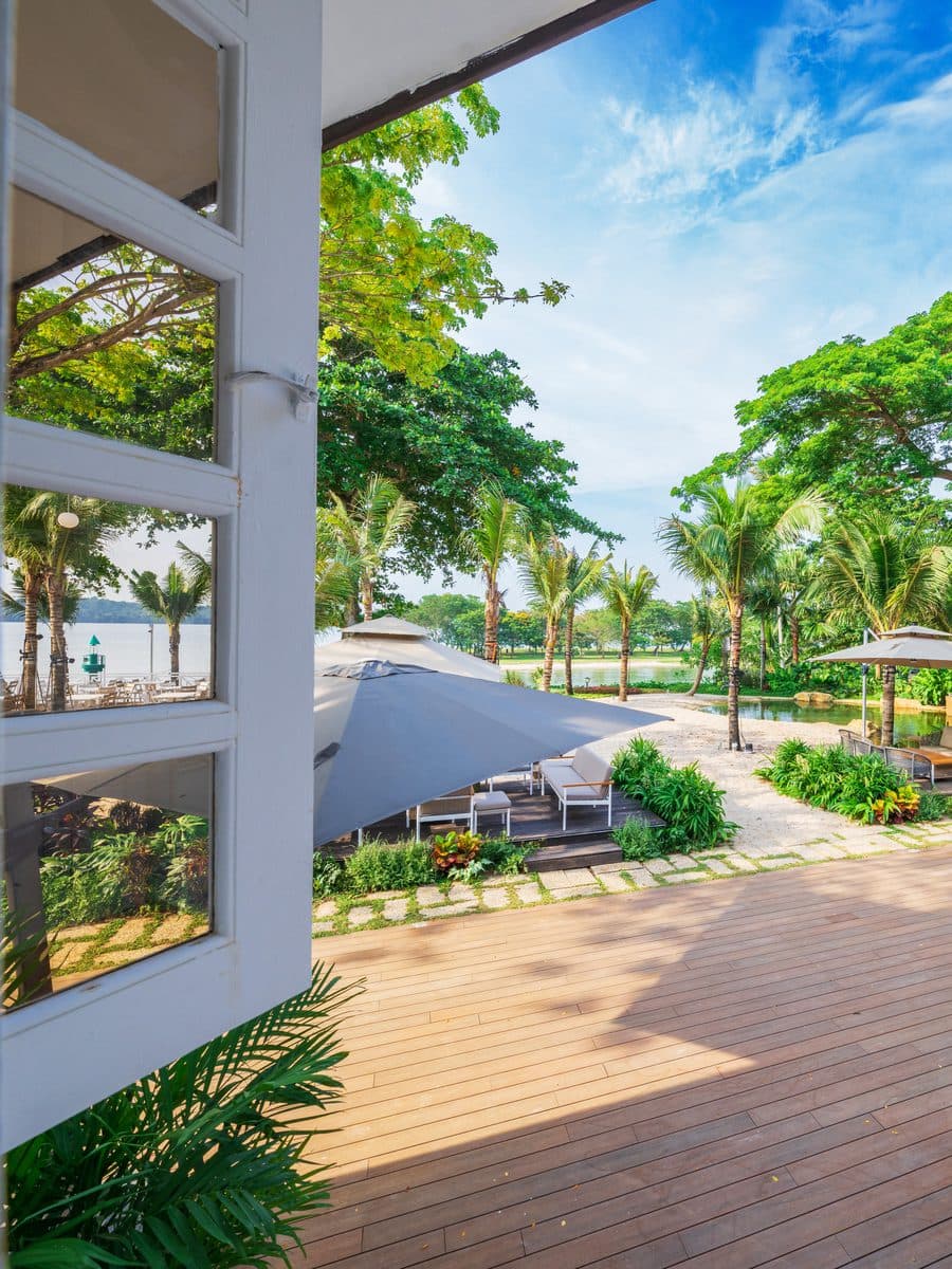 The timber deck at Canopy Changi Village, umbrellas and palms with the water beyond