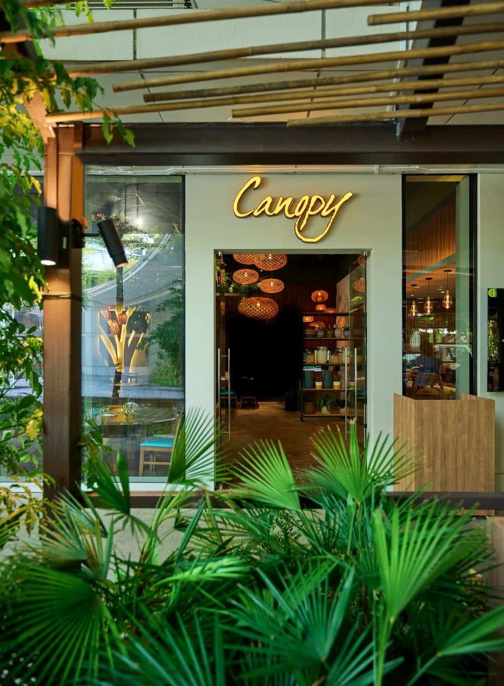 The entrance to Canopy Changi City Point, the honey wordmark above the doors behind a screen of palms