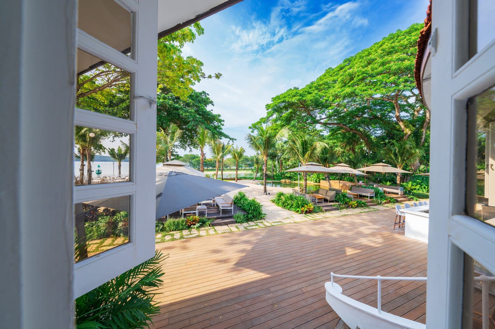 Looking out through the colonial doors at Canopy Changi Village onto the timber deck, parasols and the water beyond