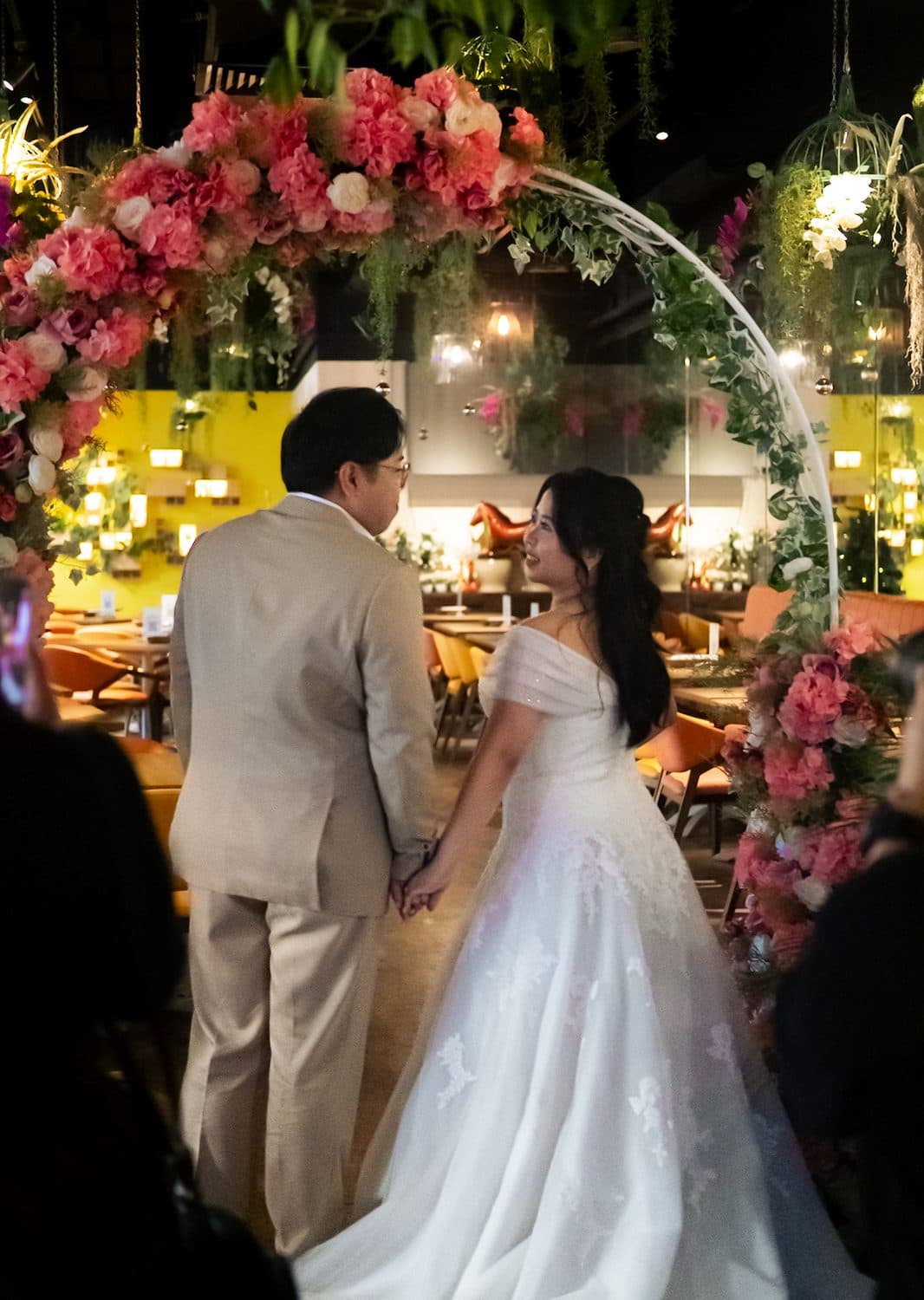 A bride and her father under a pink floral arch at an evening ceremony at Canopy Esplanade