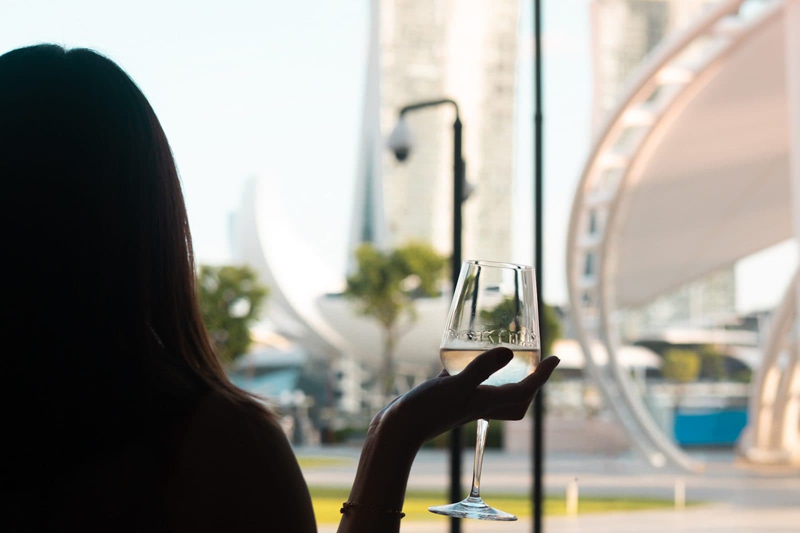 A guest at Canopy Esplanade with a glass of white, Marina Bay Sands and the Flyer across the water
