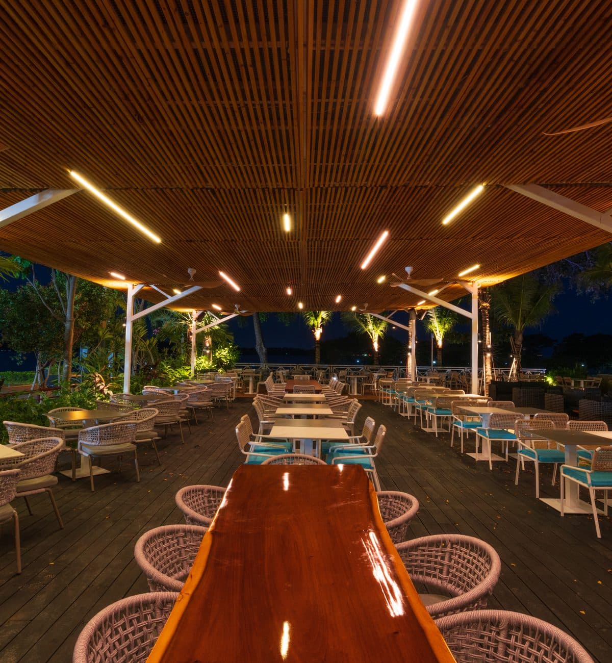 The timber pavilion at Canopy Changi Village after dark, one polished table running its length