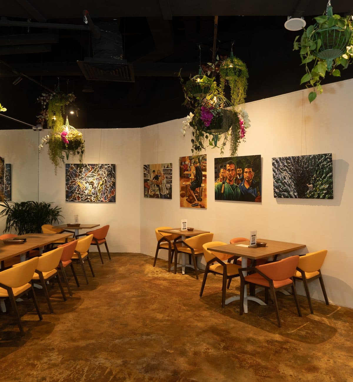 Tables at Canopy Esplanade against a white wall hung with paintings, greenery overhead