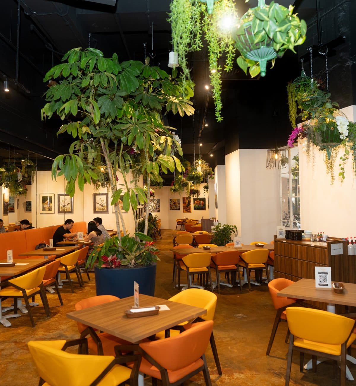 The planted dining room at Canopy Esplanade, a tree rising between the tables and artwork on the walls