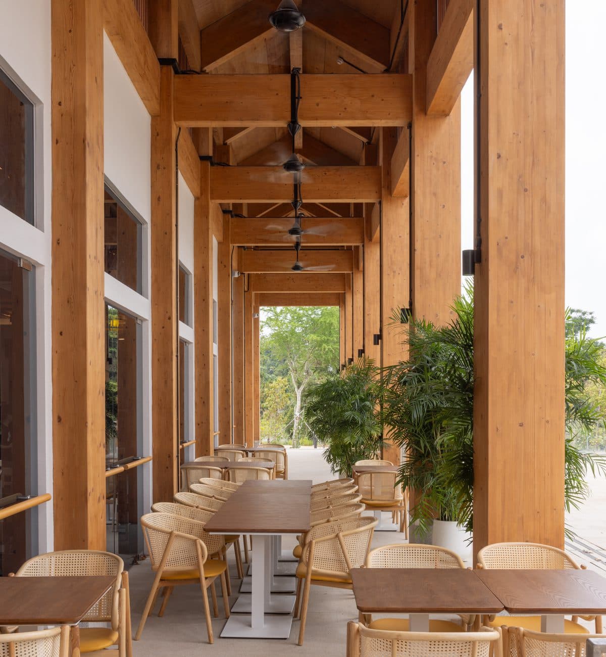 Looking down the colonnade at Canopy Jurong Lake Gardens, cane chairs and tables between the timber columns