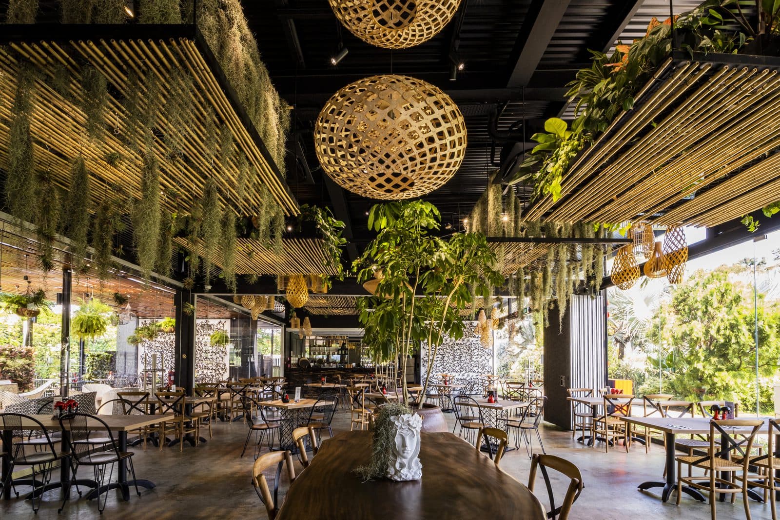 The dining room at Canopy HortPark under a bamboo ceiling, hanging greenery and woven pendant lights above a live-edge table