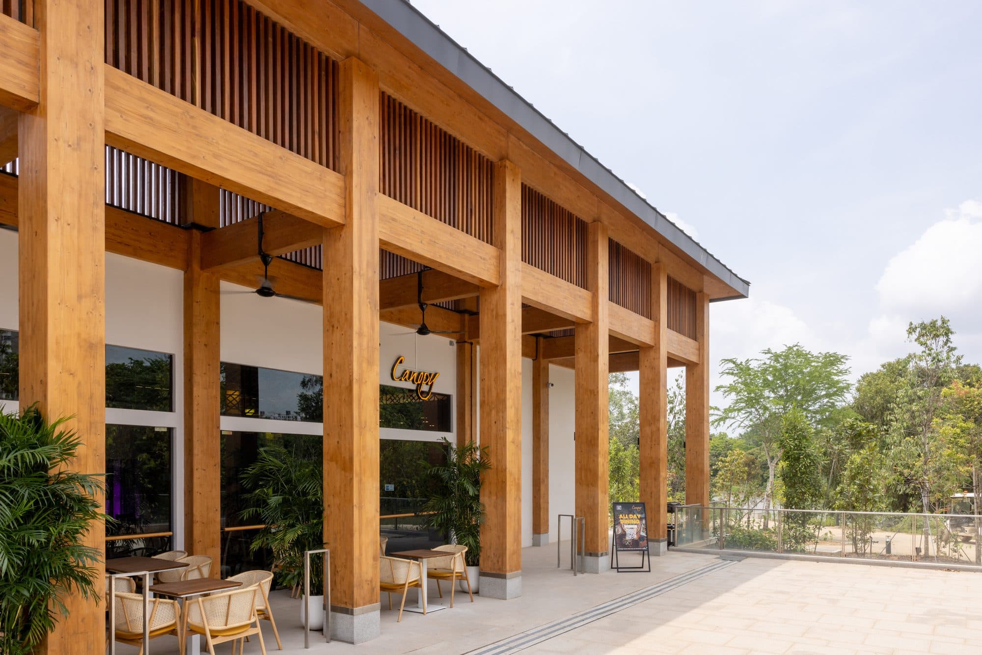 The timber colonnade running the length of Canopy Jurong Lake Gardens, alfresco tables under the eaves and the park beyond