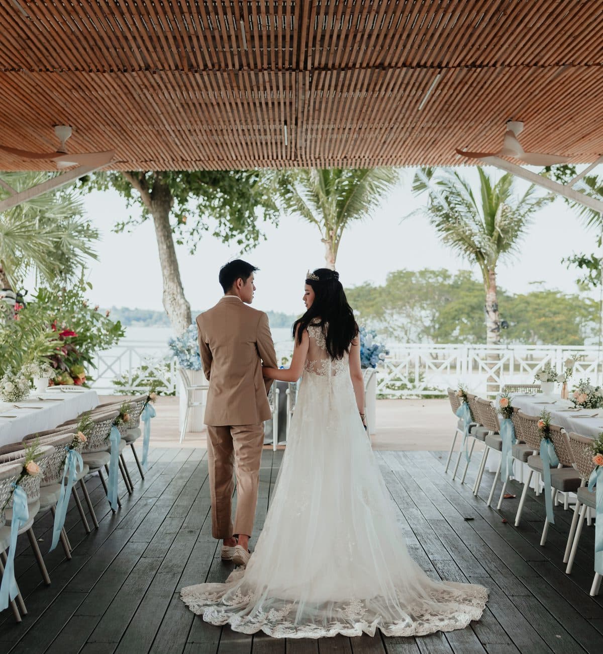 A couple walking between the long banquet tables at Canopy Changi Village, palms and the water beyond