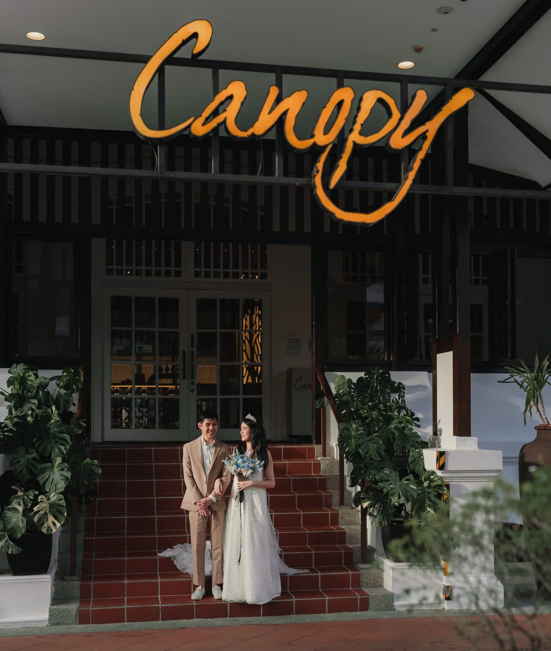 A couple on the steps under the Canopy sign at Changi Village, bouquet in hand