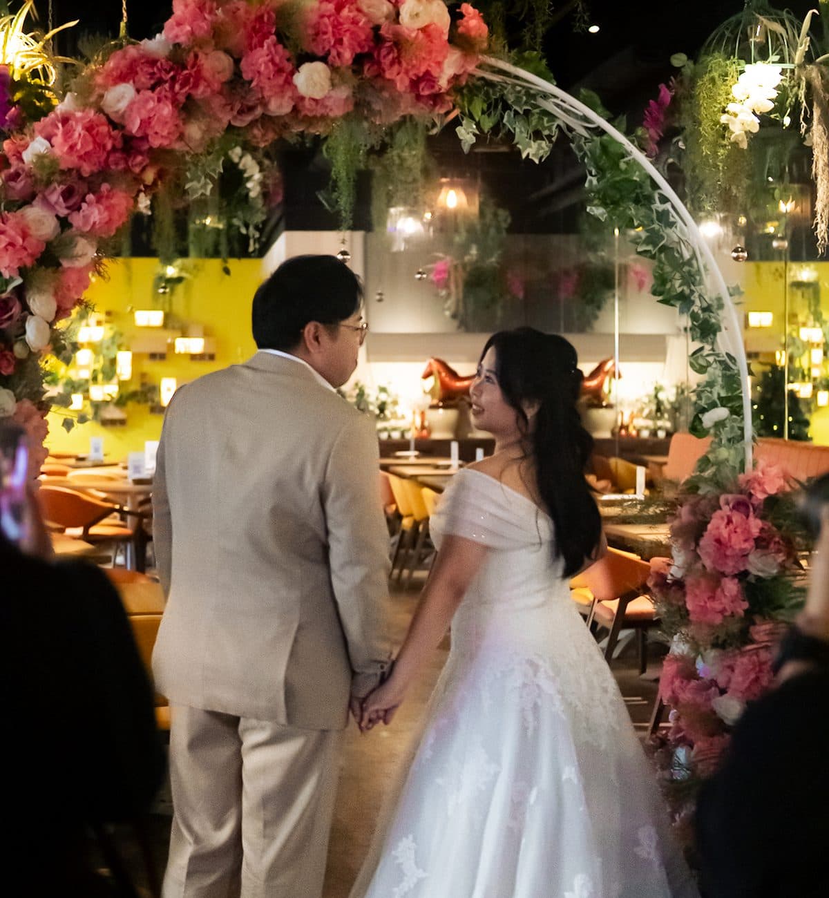 A bride and her father under a pink floral arch at an evening ceremony at Canopy Esplanade