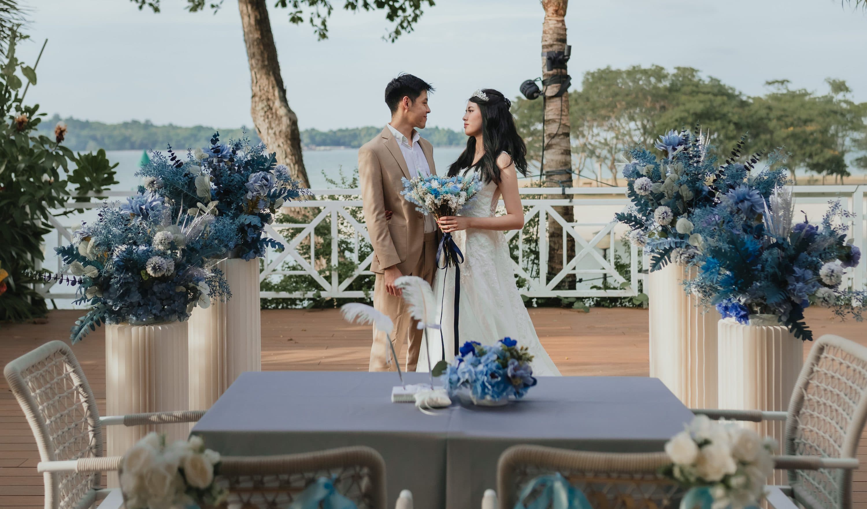 A couple by the water at Canopy Changi Village, blue florals either side of the ceremony table