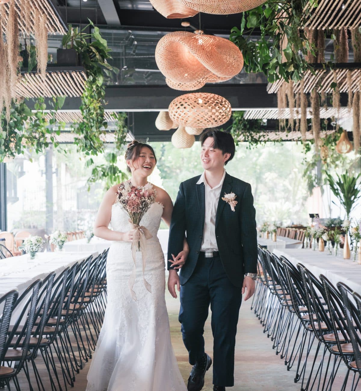 A couple walking the aisle at Canopy HortPark under rattan pendants and hanging greenery