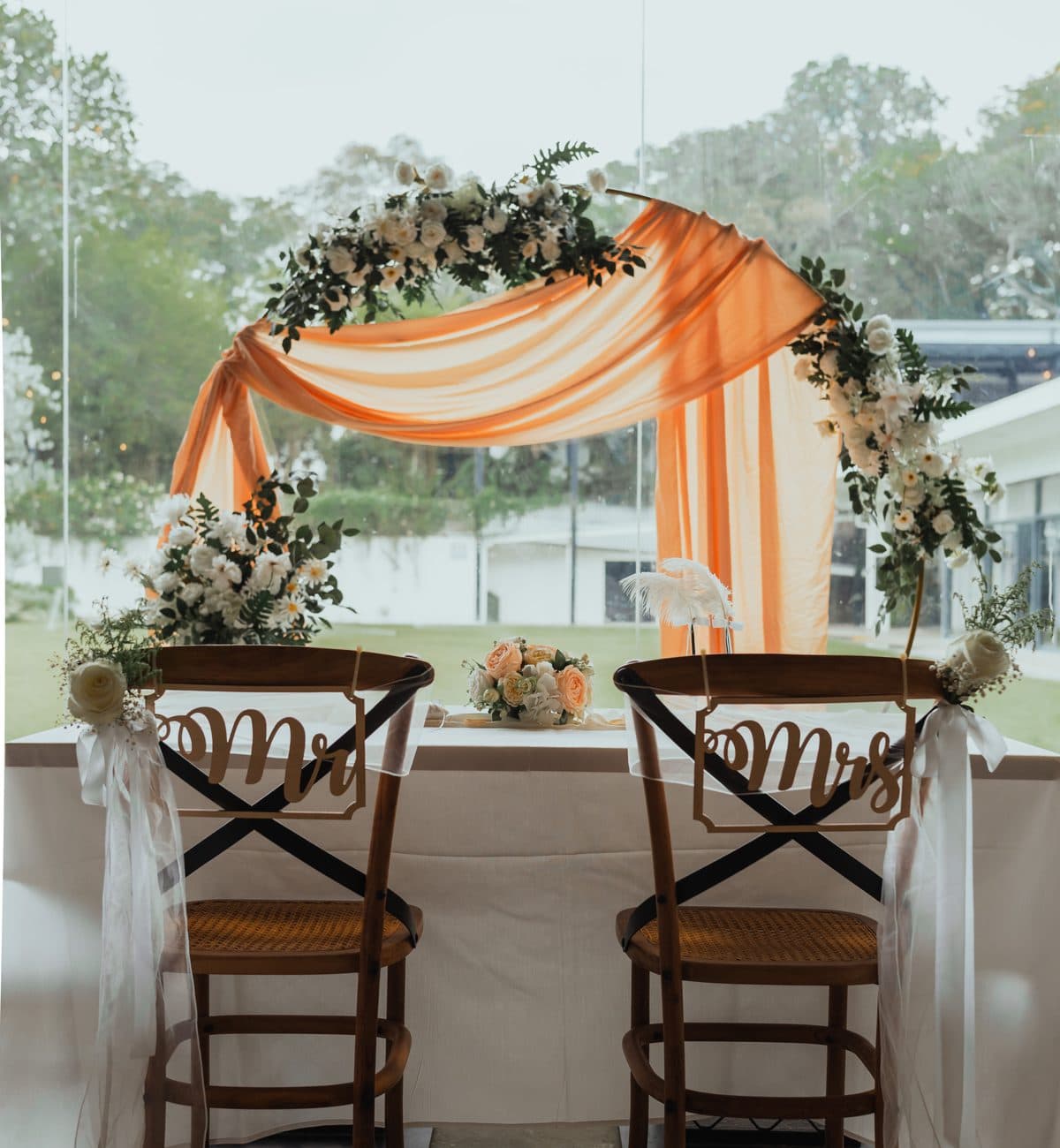 The sweetheart table at Canopy HortPark under a peach draped arch, Mr and Mrs signs on the chairs