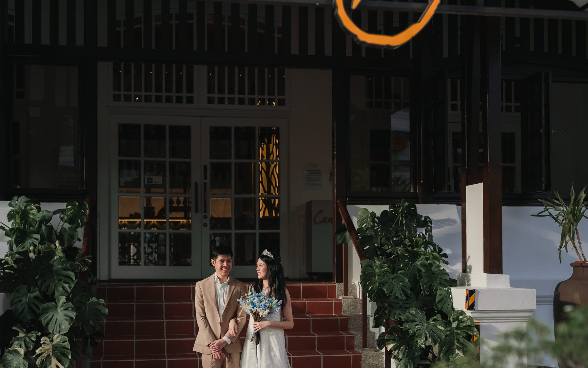 A couple on the tiled steps under the Canopy sign at Changi Village, bouquet in hand