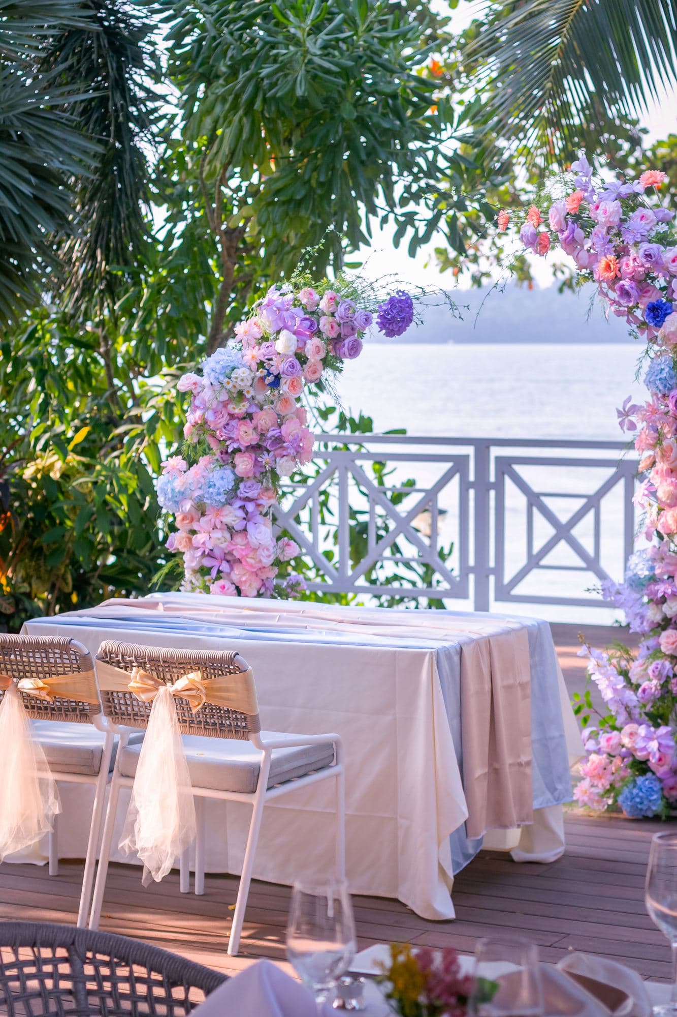 A pastel floral arch framing a table on the deck at Canopy Changi Village, the sea behind it
