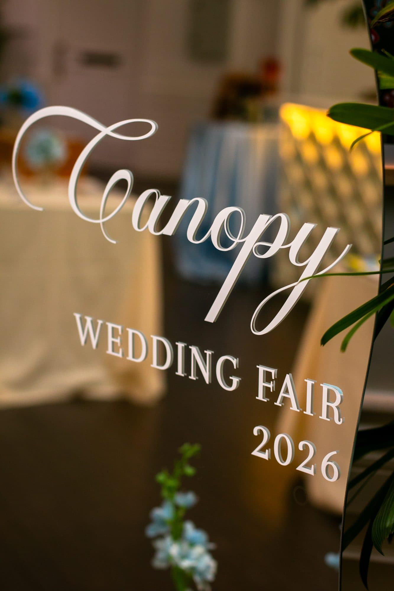 An etched mirror reading Canopy Wedding Fair 2026, foliage behind it