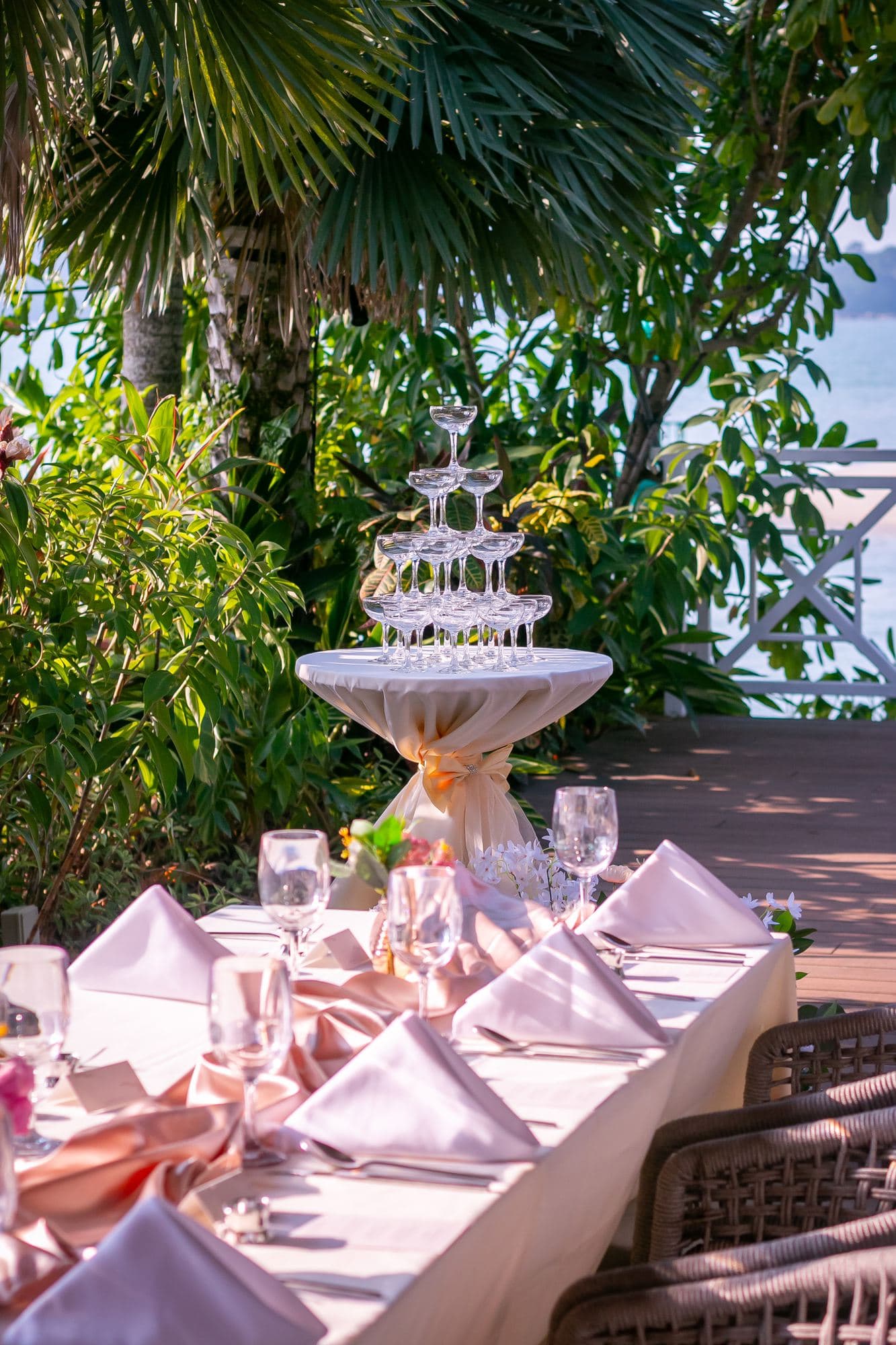 A blush table setting under the palms, a glass tower behind it